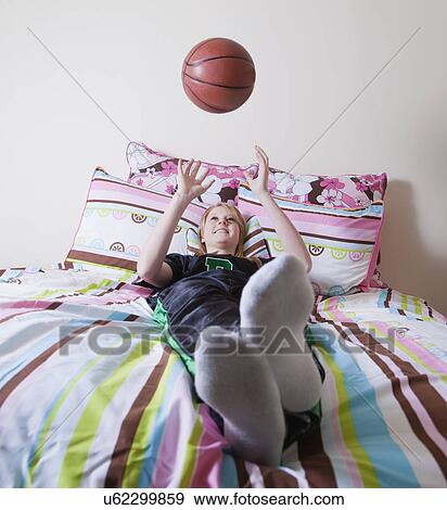 Stock Photo - USA California, Fairfax, teenage girl (14-15) lying on bed and throwing basketball. Fotosearch