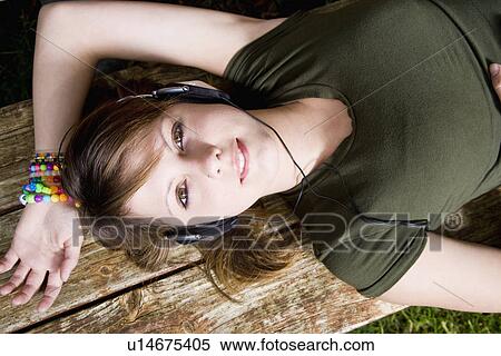 Stock Photography - USA California, Fairfax, teenage girl (16-17) lying on wooden bench and listening music. Fotosearch