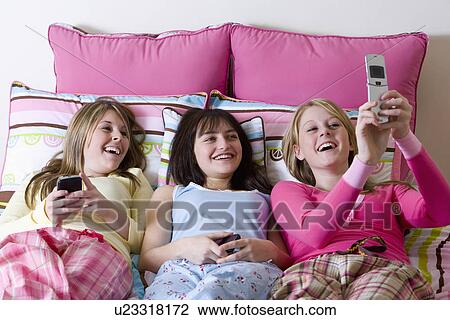 Stock Image - USA California, Fairfax, teenage girls (14-15, 16-17) lying on bed and looking at mobile phones. Fotosearch