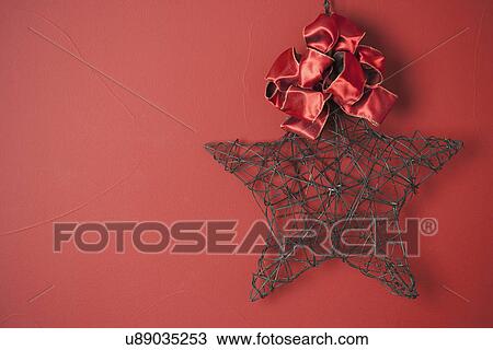 Stock Image - USA, California, La Quinta, Wire star and bow against red background. Fotosearch