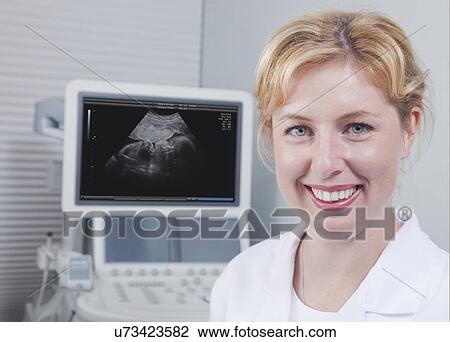Stock Image - USA California, Larkspur, Portrait of smiling woman with ultrasound monitoring system in background. Fotosearch
