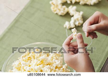 Picture - USA, California, Lawndale, Close-up of girl (10-11) sewing popcorn onto string. Fotosearch