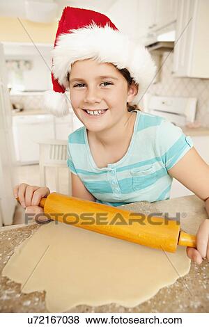 Stock Photo - USA, California, Lawndale, Girl (10-11) wearing santa hat rolling dough. Fotosearch