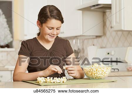 Stock Photography - USA, California, Lawndale, Girl (10-11) sewing popcorn onto string. Fotosearch
