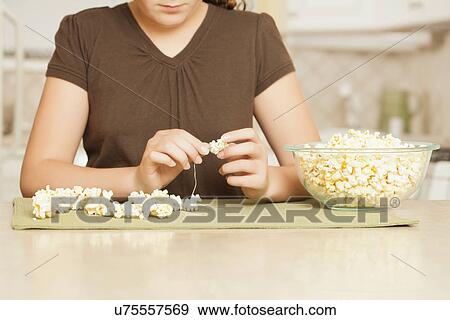 Stock Photo - USA, California, Lawndale, Midsection of girl (10-11) sewing popcorn onto string. Fotosearch