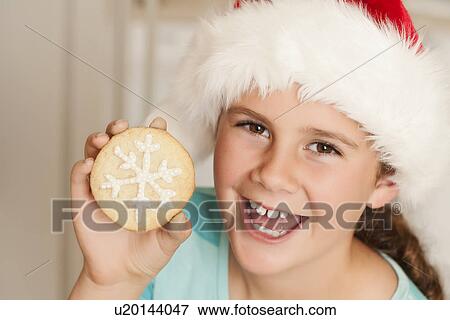Stock Photo - USA, California, Lawndale, Portrait of girl (10-11) wearing santa hat holding cookie. Fotosearch