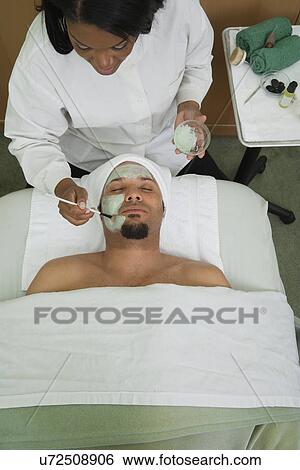 Stock Photograph - USA, California, Oakland, beautician applying facial mask on man's face in spa. Fotosearch
