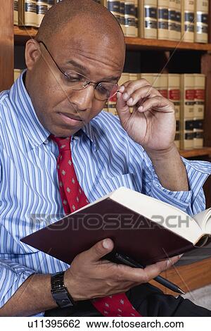 Stock Image - USA, California, Oakland, Man reading books in library. Fotosearch