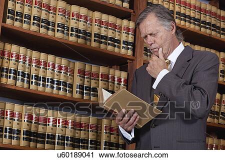 Stock Image - USA, California, Oakland, Man reading books in library. Fotosearch