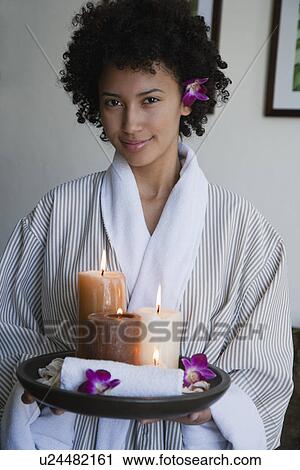 Stock Image - USA, California, Oakland, portrait of young woman holding plate with candles and orchids. Fotosearch