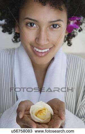 Stock Image - USA, California, Oakland, portrait of young woman holding yellow rose. Fotosearch
