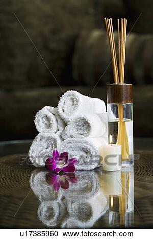 Stock Image - USA, California, Oakland, rolled up towels, aroma sticks, candle and orchid on table. Fotosearch