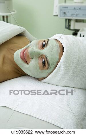 Stock Image - USA, California, Oakland, smiling young woman with facial mask lying on massage bed. Fotosearch