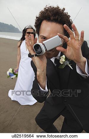 Picture - USA, California, San Francisco, Baker Beach, bride and groom with camcorder on beach. Fotosearch