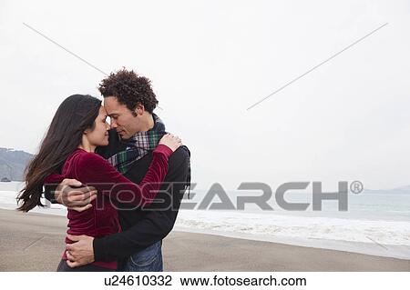 Stock Image - USA, California, San Francisco, Baker Beach, couple embracing on beach. Fotosearch