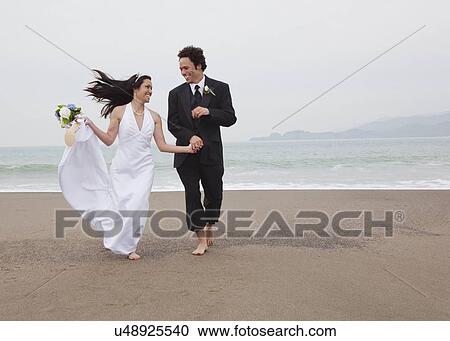 Stock Image - USA, California, San Francisco, Baker Beach, bride and groom walking on beach. Fotosearch