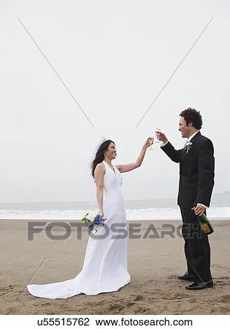 Stock Image - USA, California, San Francisco, Baker Beach, bride and groom toasting on beach. Fotosearch