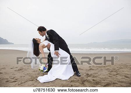 Stock Image - USA, California, San Francisco, Baker Beach, bride and groom dancing on beach. Fotosearch