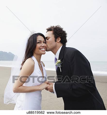 Stock Image - USA, California, San Francisco, Baker Beach, bride and groom kissing on beach. Fotosearch