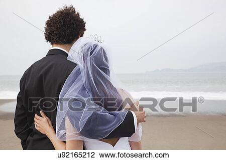 Stock Image - USA, California, San Francisco, Baker Beach, bride and groom standing on beach. Fotosearch