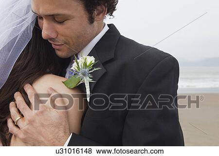 Stock Photo - USA, California, San Francisco, Baker Beach, bride and groom embracing on beach. Fotosearch