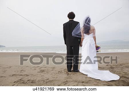 Stock Photo - USA, California, San Francisco, Baker Beach, bride and groom standing on beach. Fotosearch