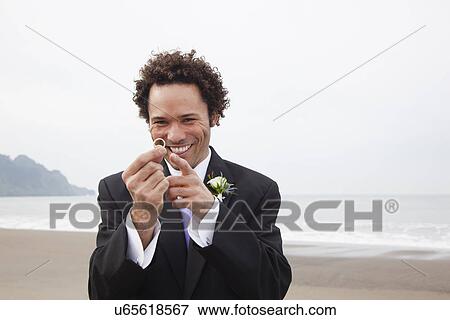 Stock Photo - USA, California, San Francisco, Baker Beach, portrait of groom on beach holding ring. Fotosearch
