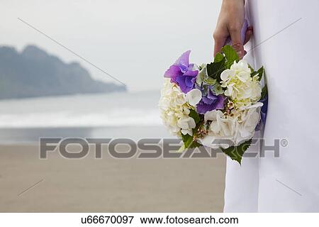 Stock Photo - USA, California, San Francisco, Baker Beach, midsection of bride with bouquet on beach. Fotosearch