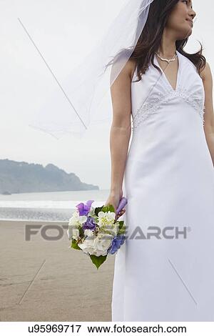 Stock Photo - USA, California, San Francisco, Baker Beach, bride with bouquet on beach. Fotosearch