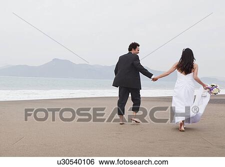 Stock Photograph - USA, California, San Francisco, Baker Beach, bride and groom walking on beach. Fotosearch
