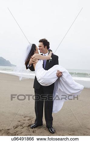 Stock Photograph - USA, California, San Francisco, Baker Beach, bride and groom embracing on beach. Fotosearch