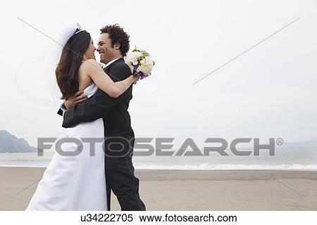 Stock Photography - USA, California, San Francisco, Baker Beach, bride and groom embracing on beach. Fotosearch