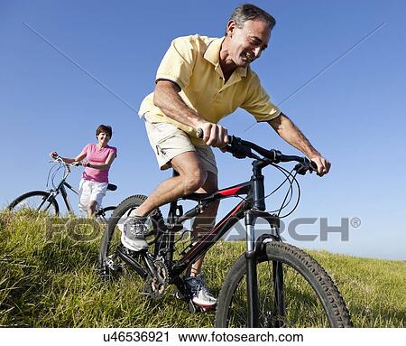 Stock Image - USA, California, San Francisco, Couple cycling among meadow. Fotosearch