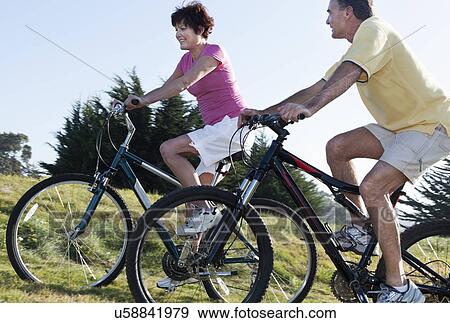 Stock Photo - USA, California, San Francisco, Couple cycling among meadow. Fotosearch