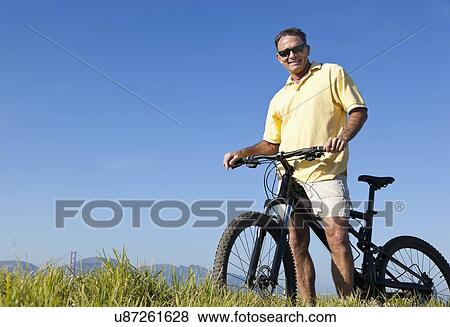 Stock Photo - USA, California, San Francisco, Cyclist standing against blue sky. Fotosearch