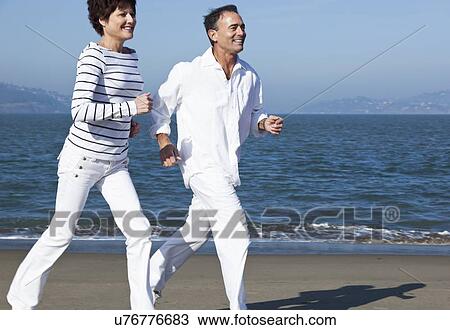 Stock Image - USA, California, San Francisco, Elder couple jogging on beach. Fotosearch