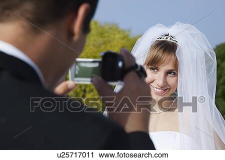 Stock Image - USA, California, San Francisco, groom filming bride outdoors. Fotosearch
