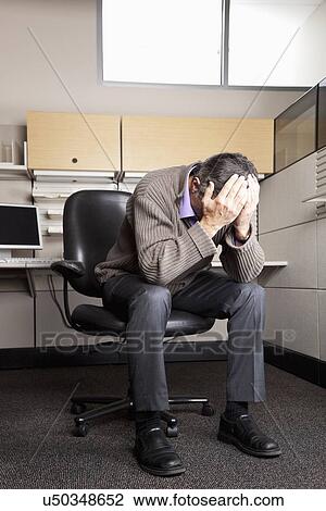 Stock Image - USA, California, San Rafael, business man with head in hands sitting in office. Fotosearch