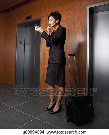 Picture - USA, California, San Rafael, Businesswoman applying lipstick in corridor. Fotosearch