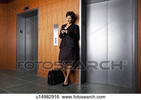 Stock Photograph - USA, California, San Rafael, Businesswoman text-messaging in corridor. Fotosearch