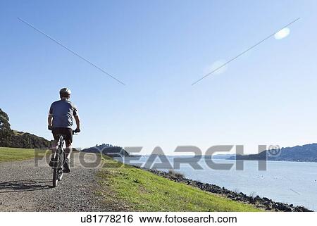 Stock Photograph - USA, California, Tiburon, Cyclist at lakeside. Fotosearch