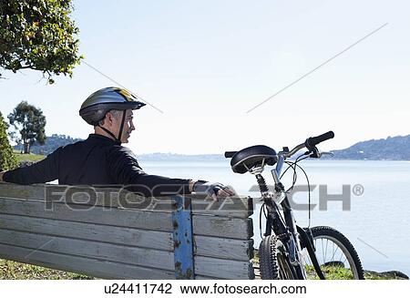 Stock Image - USA, California, Tiburon, Cyclist resting on bench at lakeside. Fotosearch