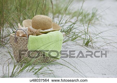 Picture - USA, Florida, St. Pete Beach, Basket with straw hat, towel and shells on beach. Fotosearch