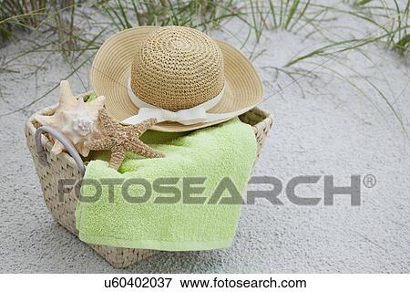 Stock Photo - USA, Florida, St. Pete Beach, Basket with straw hat, towel and shells on beach. Fotosearch