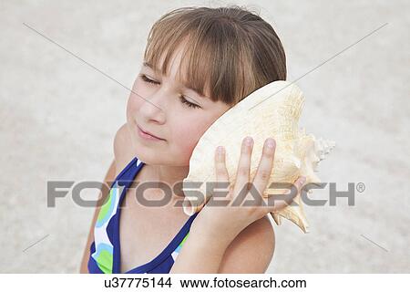 Picture - USA, Florida, St. Pete Beach, Girl (8-9) listening to conch shell on beach. Fotosearch