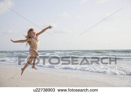 Stock Image - USA, Florida, St. Pete Beach, Girl (8-9) in bikini jumping on beach. Fotosearch