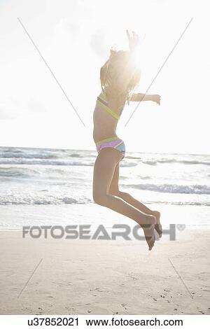 Stock Image - USA, Florida, St. Pete Beach, Girl (8-9) in bikini jumping on beach. Fotosearch