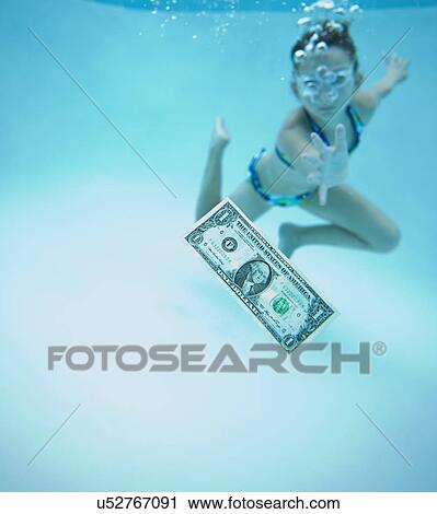 Stock Image - USA, Florida, St. Pete Beach, Girl (8-9) swimming in pool and reaching for one dollar banknote. Fotosearch