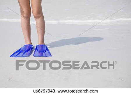 Stock Image - USA, Florida, St. Pete Beach, Girl (8-9) with flippers standing on beach, low section. Fotosearch