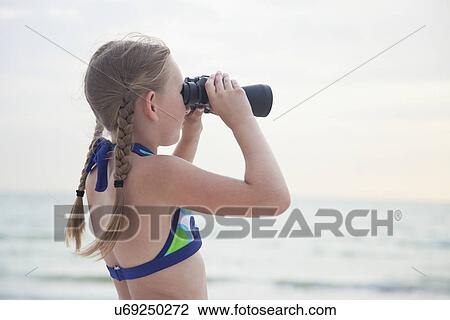 Stock Image - USA, Florida, St. Pete Beach, Girl (8-9) looking through binoculars on beach. Fotosearch